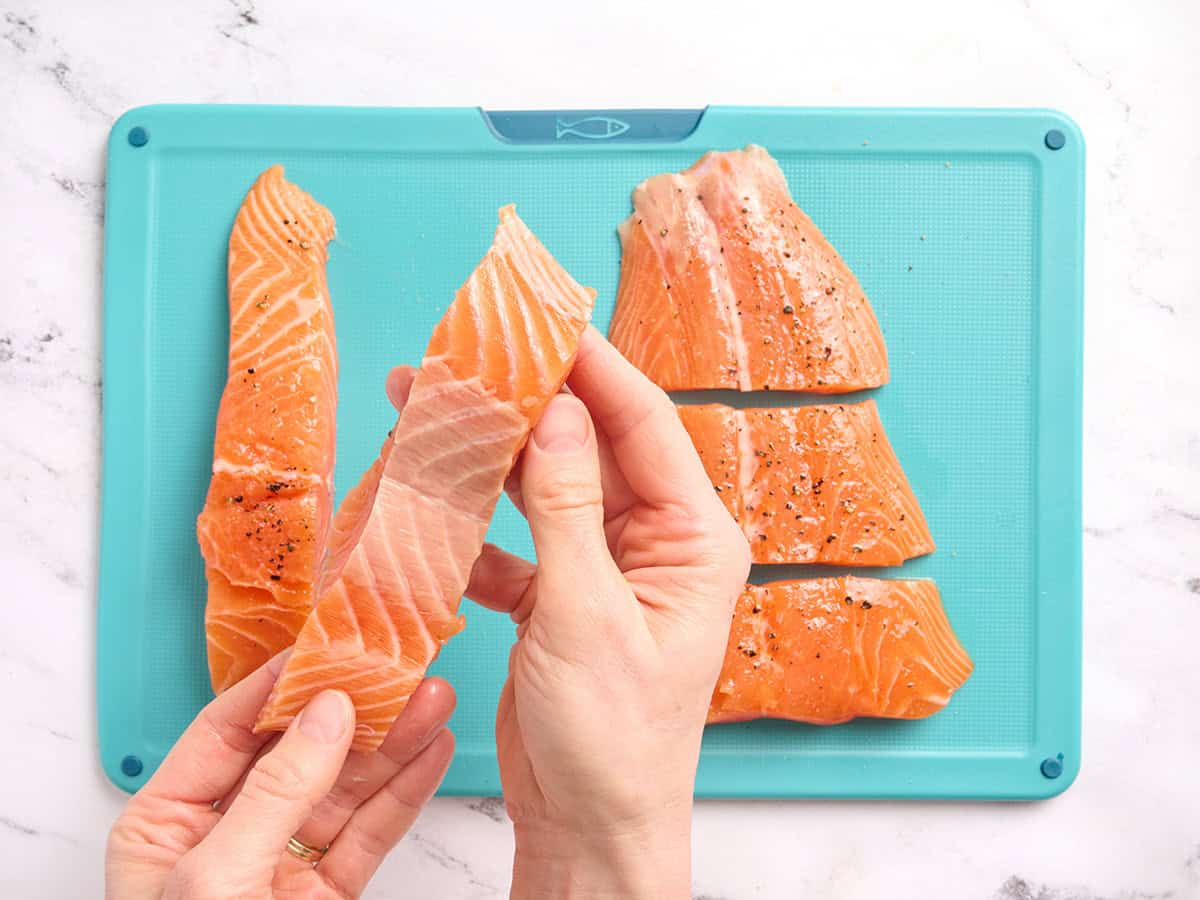 Manos sosteniendo un trozo de salmón que muestra cómo se ve sin la piel.