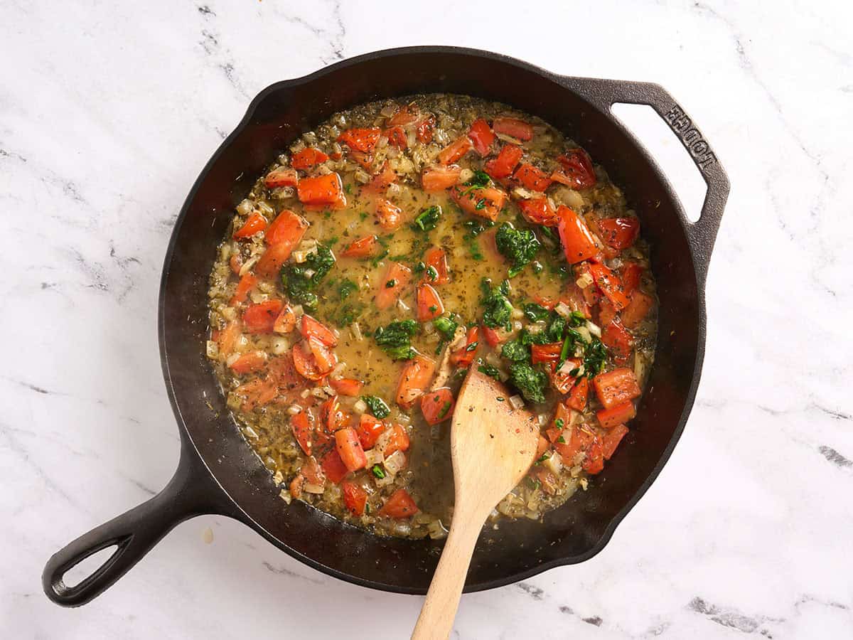 Espinacas congeladas agregadas a una sartén con tomates, cebollas y caldo.