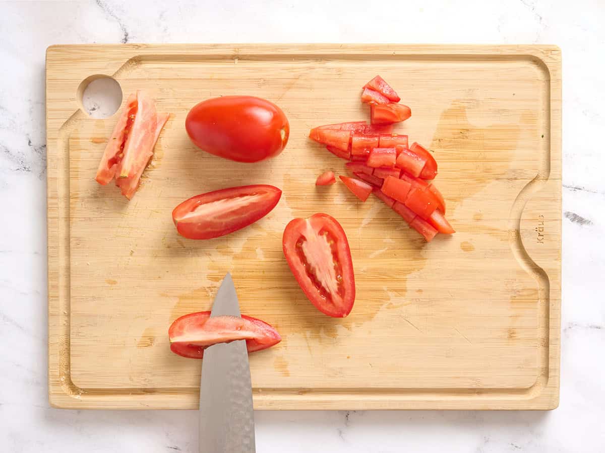 Tomates Roma cortados en cuartos sobre una tabla de cortar de madera, quitando las semillas con un cuchillo.