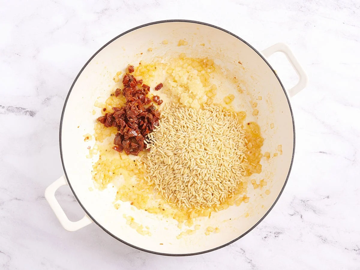 Orzo, tomates secos cortados en cubitos y ajo en una sartén.