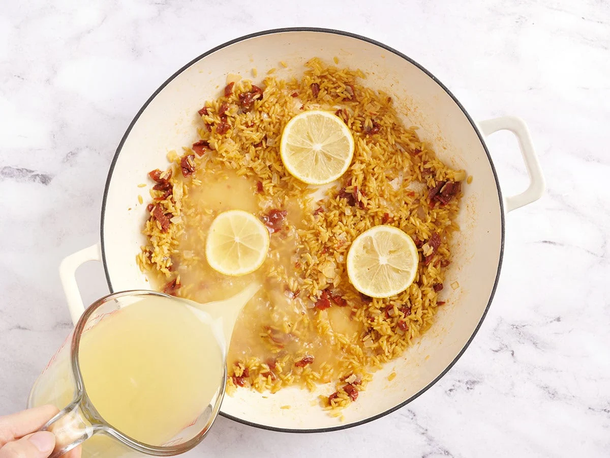 Rodajas de limón y cebolla en una sartén con caldo de pollo.