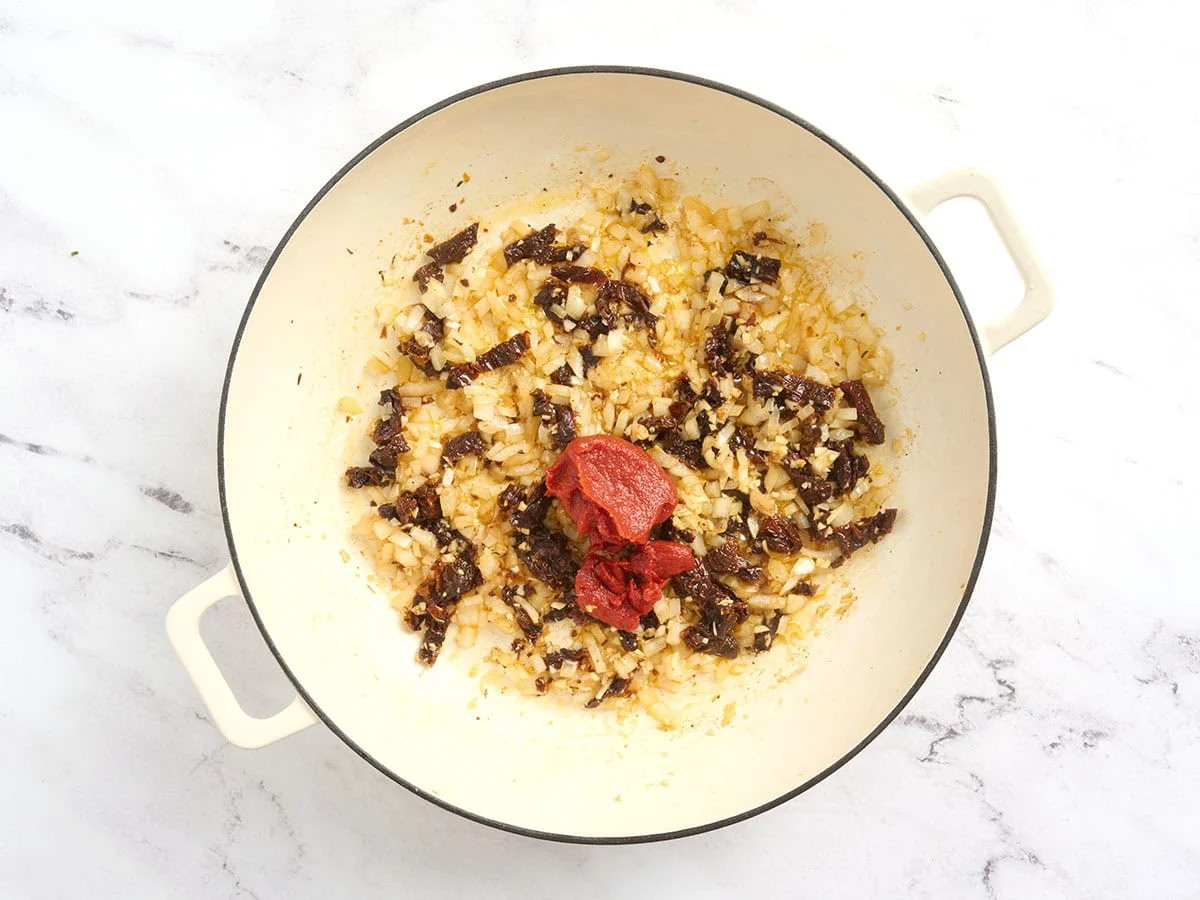 Pasta de tomate agregando a una olla con cebollas salteadas.