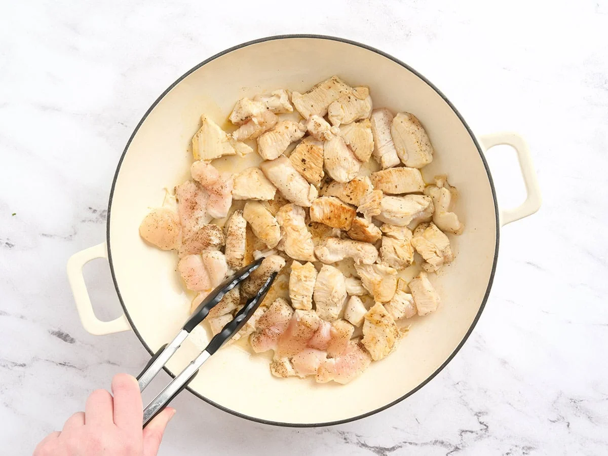Pinzas de cocina volteando trozos de pollo en una olla.