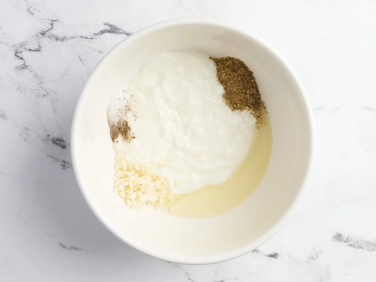 Yogur, aceite, hierbas y ajo en un bol para hacer una marinada griega.