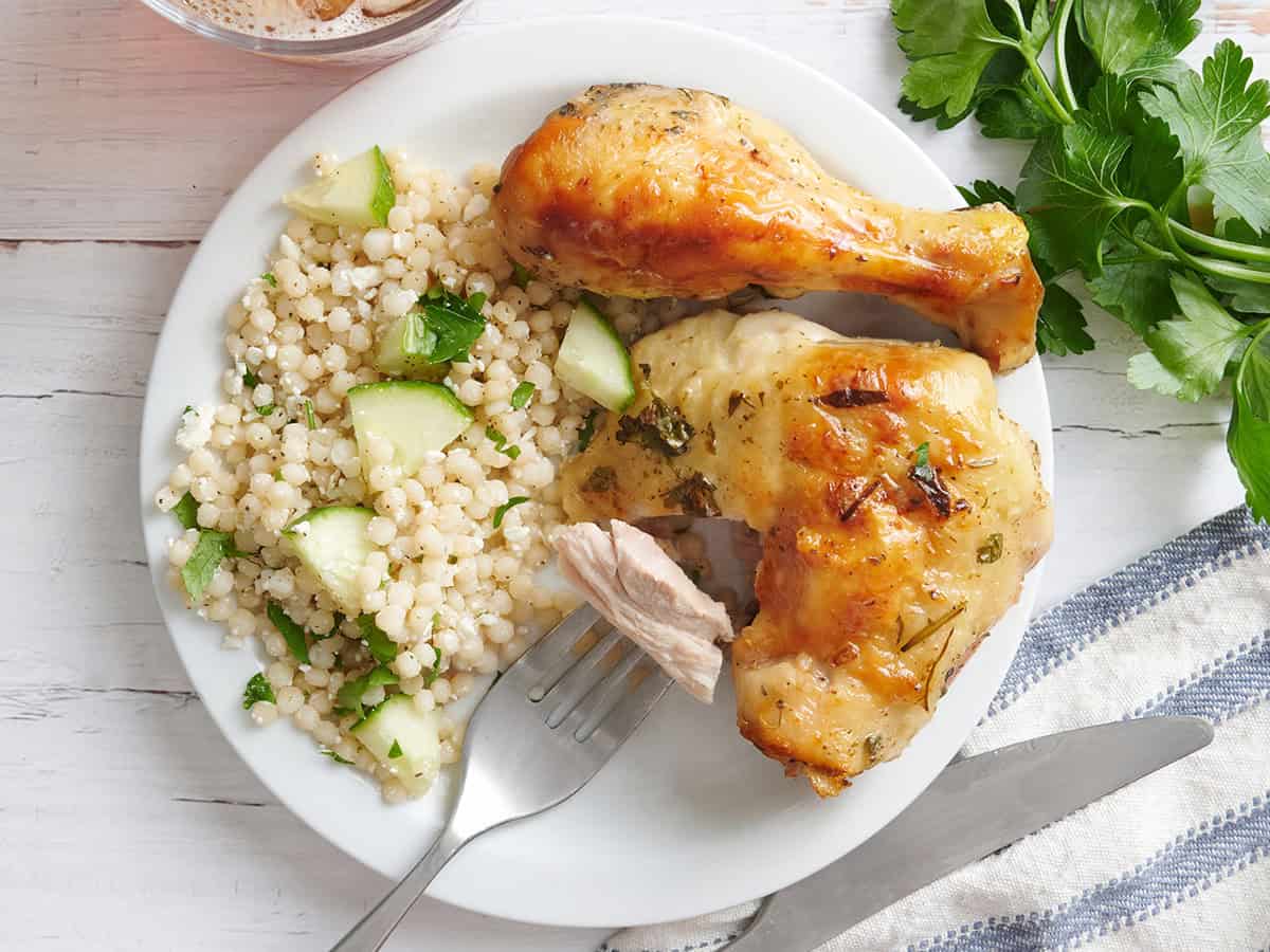 Vista aérea de un plato de pollo griego marinado con cuscús y un tenedor con un poco de pollo.