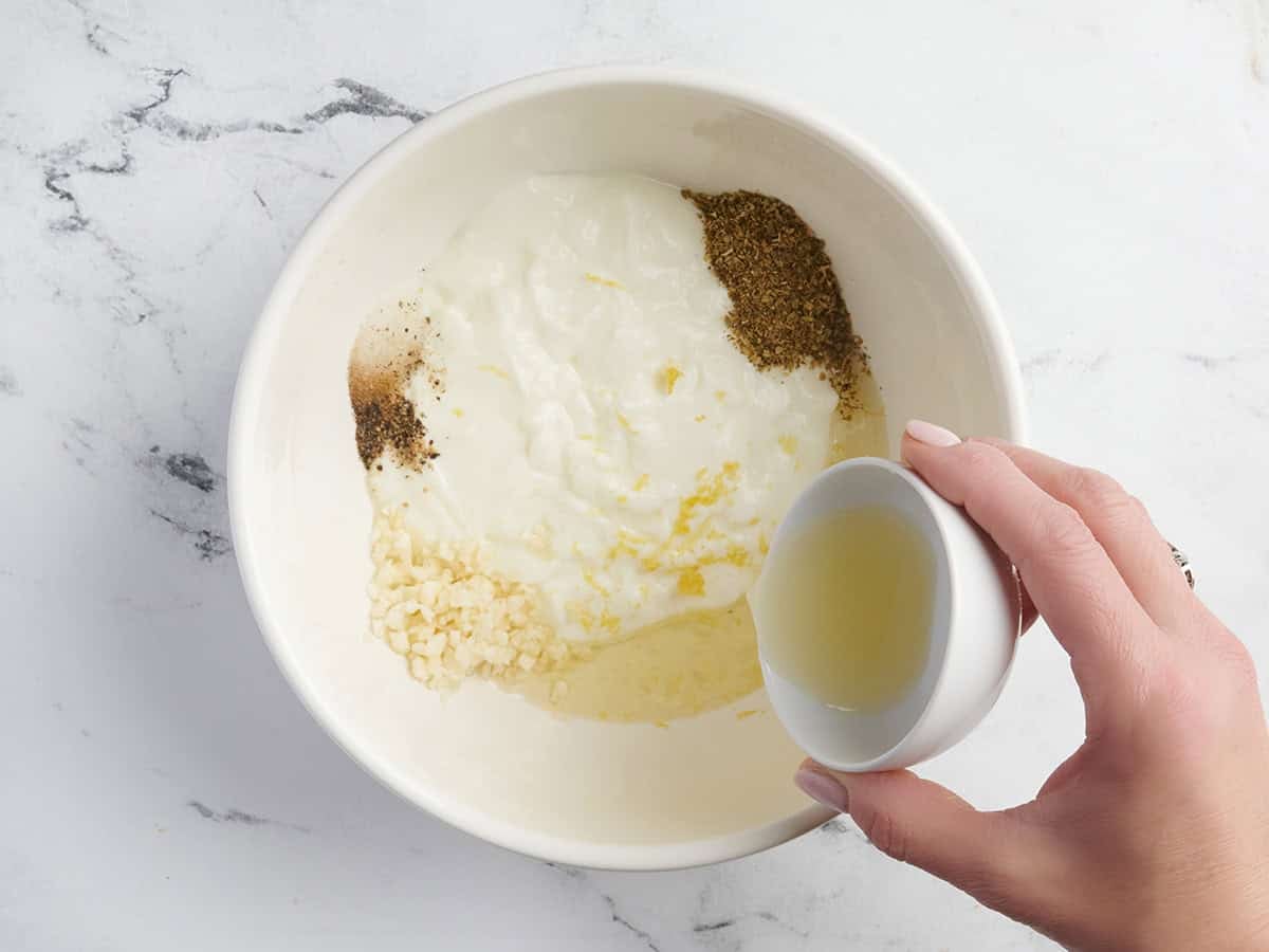 Se vierte jugo de limón en un bol con yogur, ajo y hierbas.