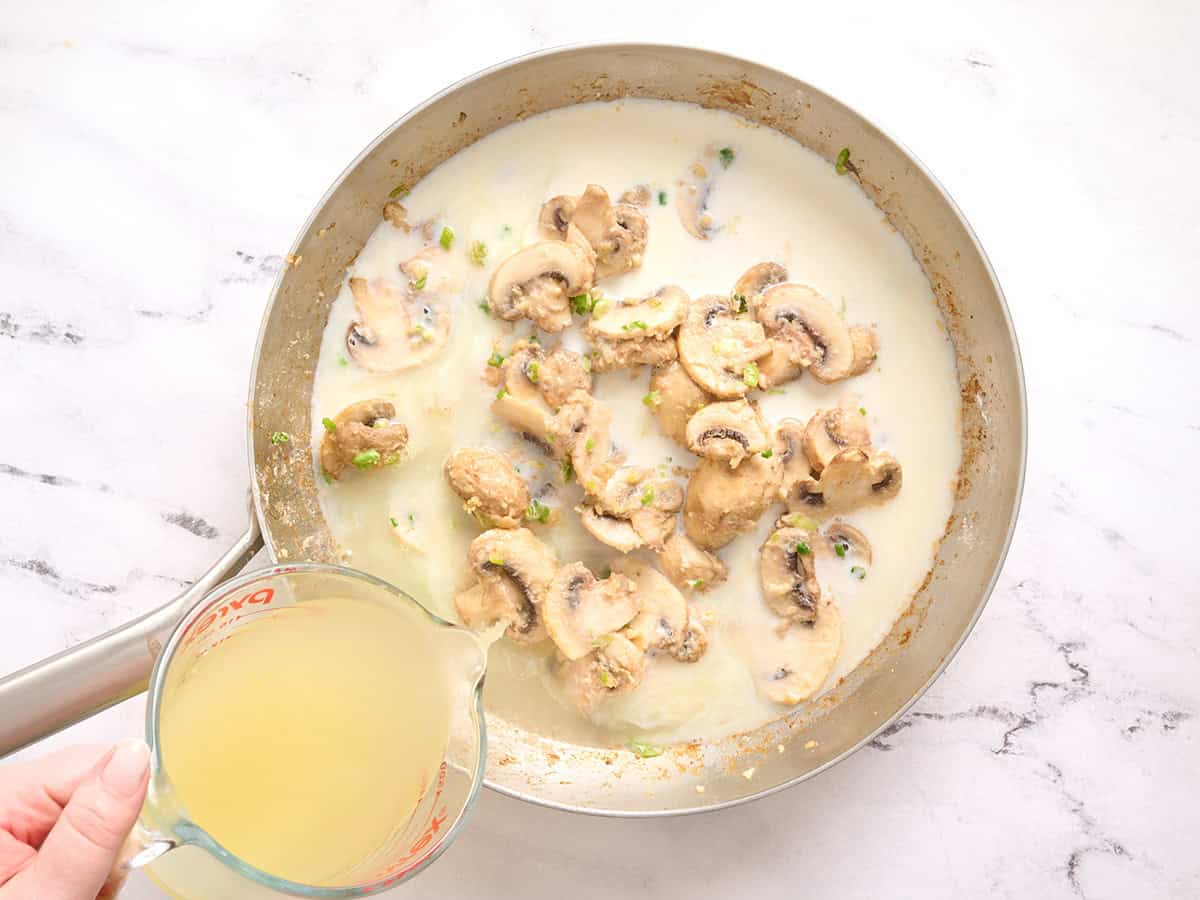 Se vierte caldo de pollo en una sartén con champiñones y leche.