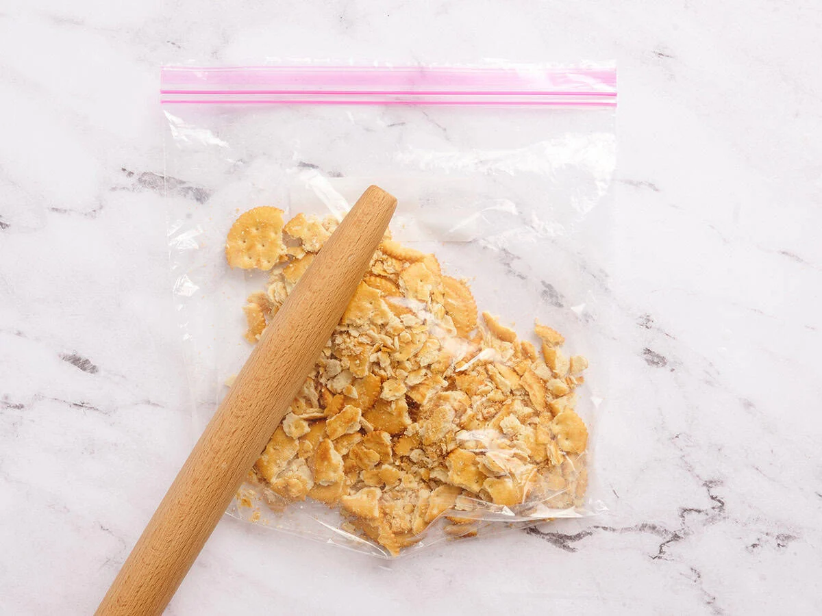 Galletas saladas en una bolsa con cierre que se trituran con un rodillo.