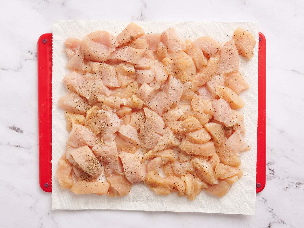 Pollo cortado en cubitos sobre una alfombrilla para cortar.