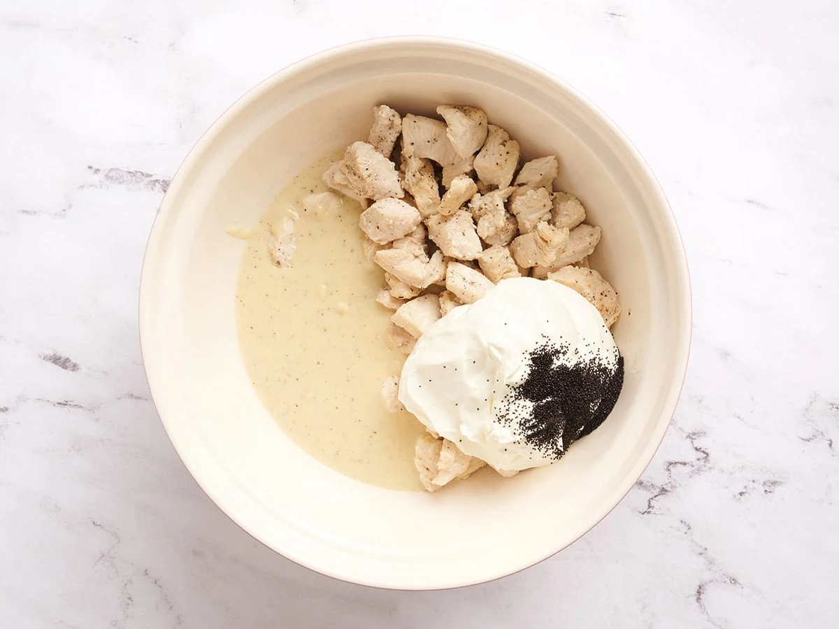 Un tazón para mezclar con pollo, crema agria, semillas de amapola y salsa en un tazón.