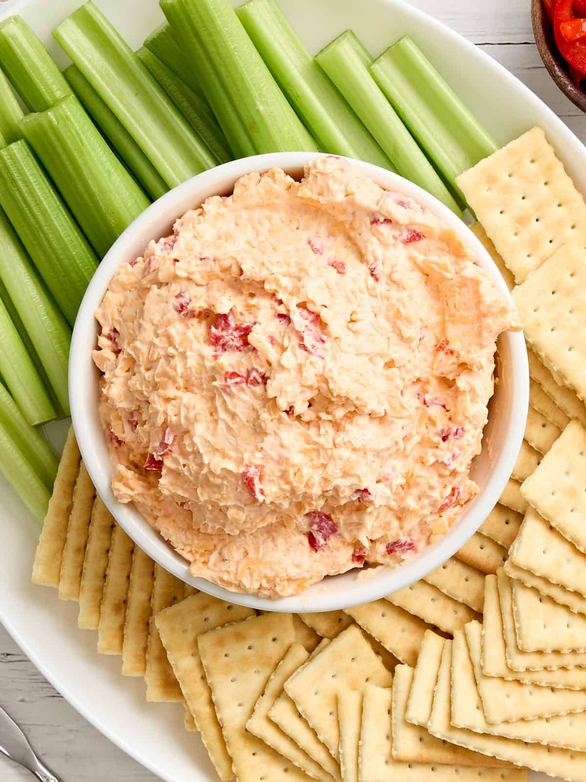 Vista aérea de un plato de queso pimiento con apio y galletas saladas.