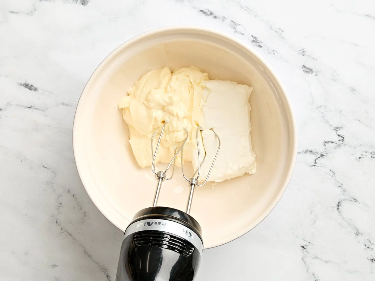 Mayo y queso crema en un bol con batidora de mano.