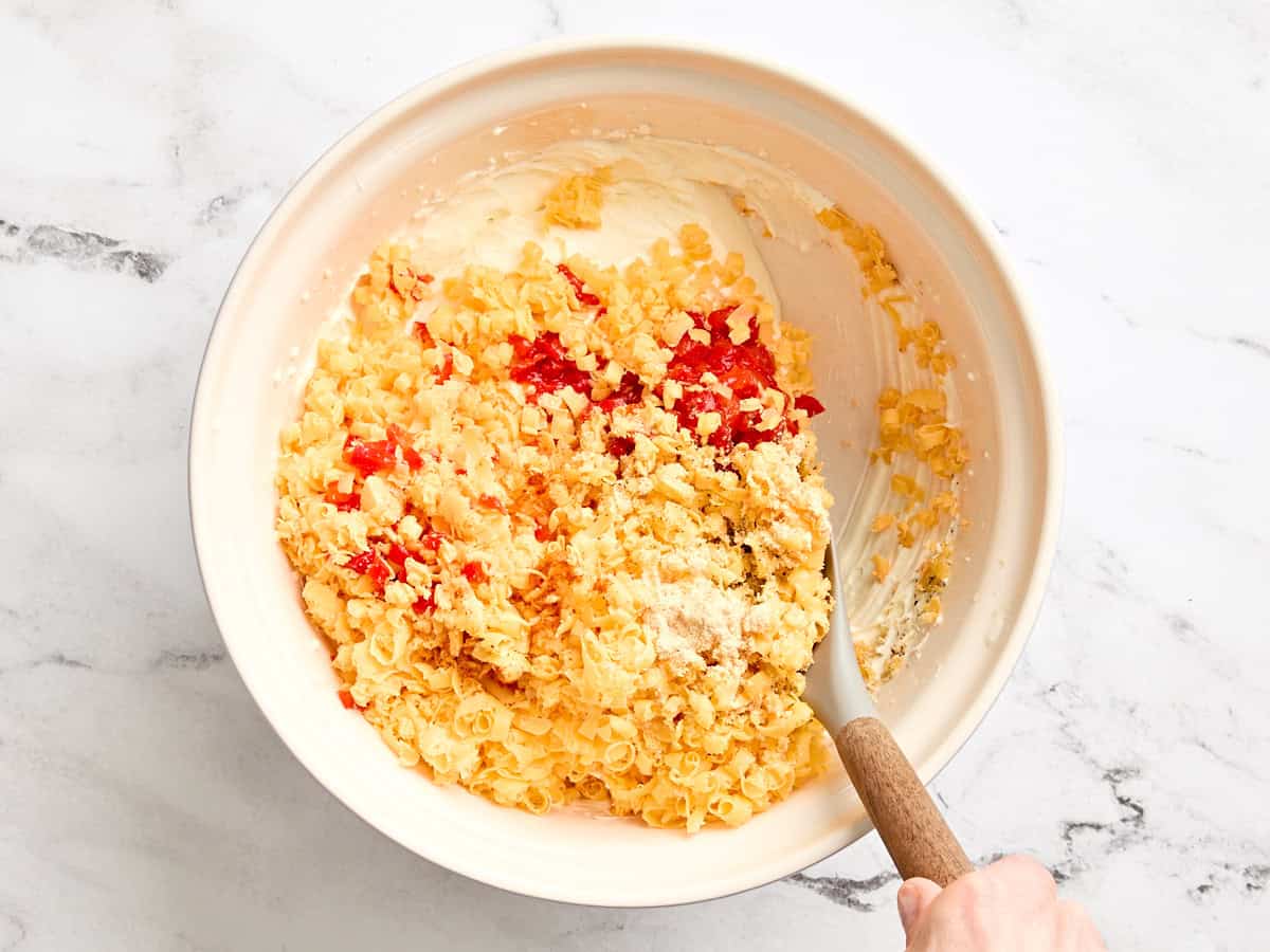 El queso cheddar rallado y los pimientos picados se agregan a un tazón de mayonesa y queso crema combinados.