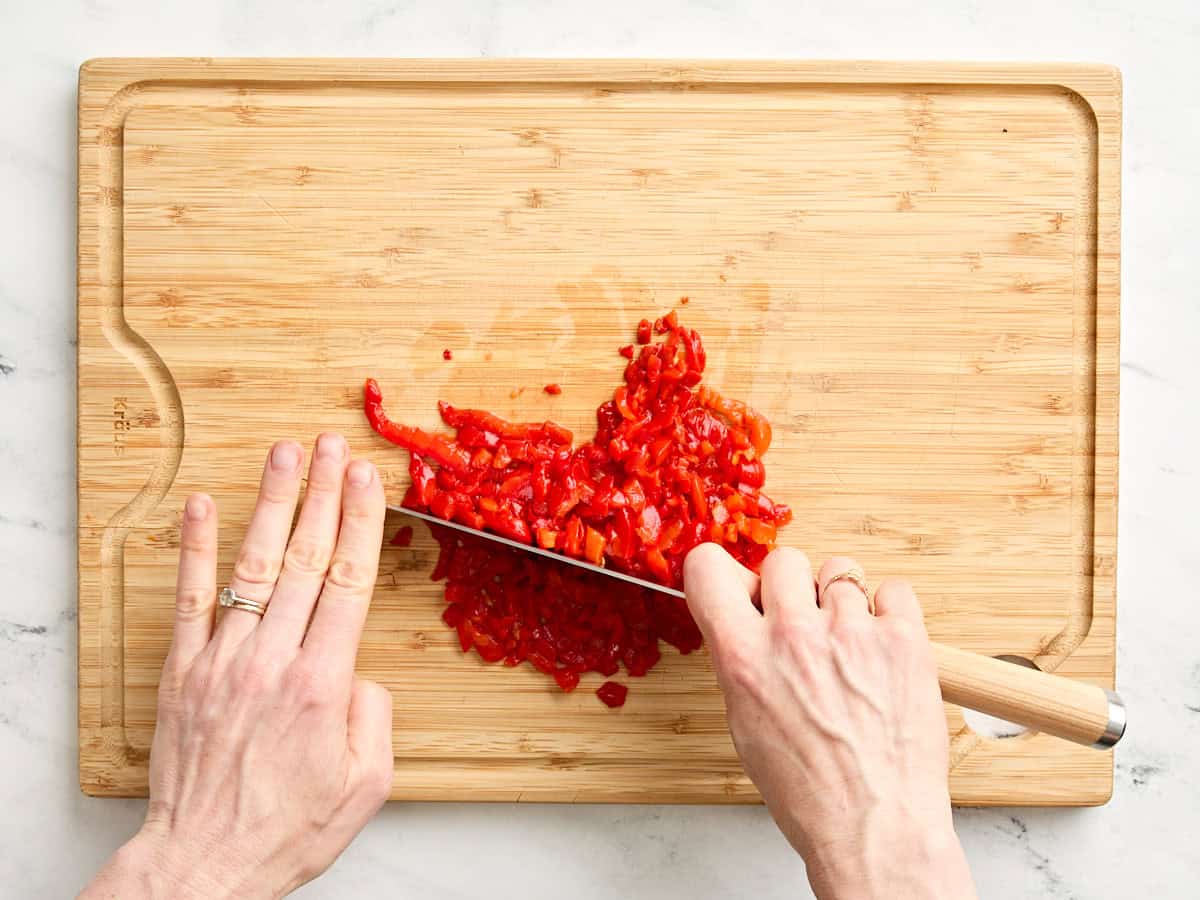 Manos usando un cuchillo para picar pimientos morrones.
