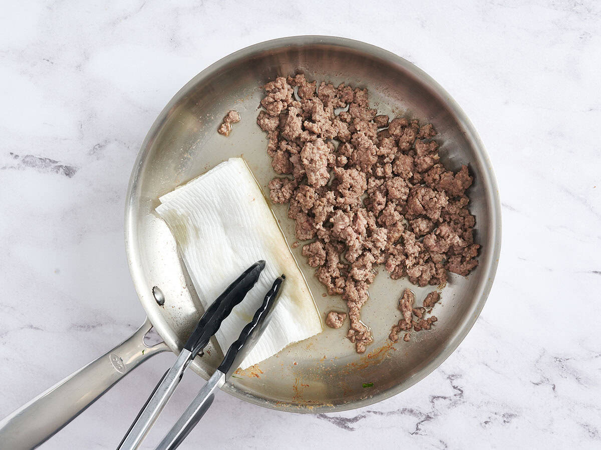 Una toalla de papel limpiando la grasa de una sartén con carne molida.