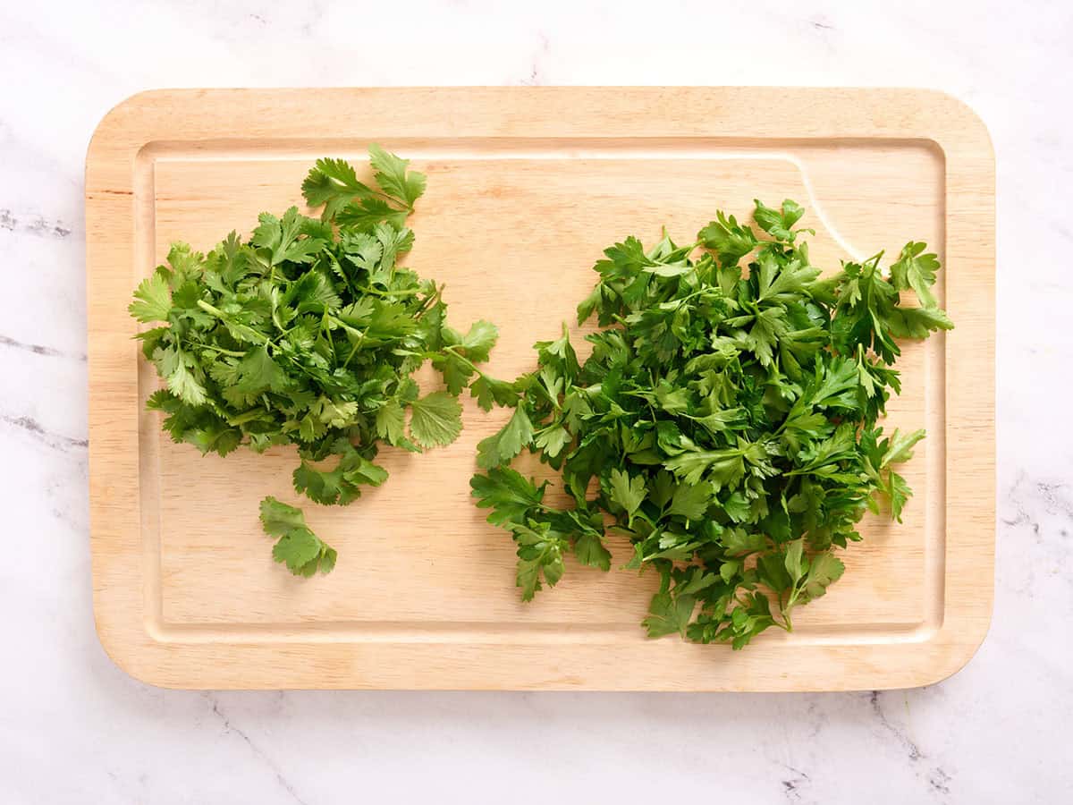 Cilantro y perejil sobre una tabla para cortar.