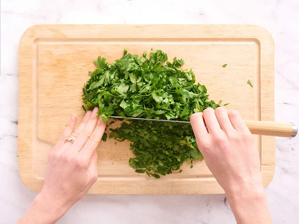 Manos usando un cuchillo para picar cilantro y perejil frescos.