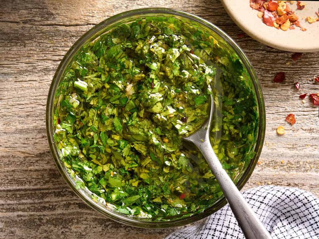 Overhead view of a bowl of chimichurri sauce with a spoon.