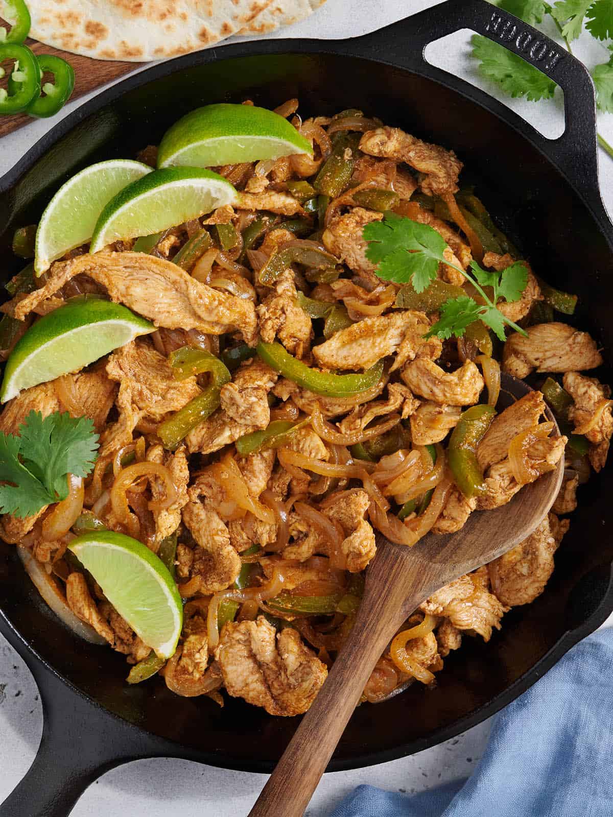 Vista aérea de una fajita de pollo al horno que se rellena en una sartén con una cuchara de madera.