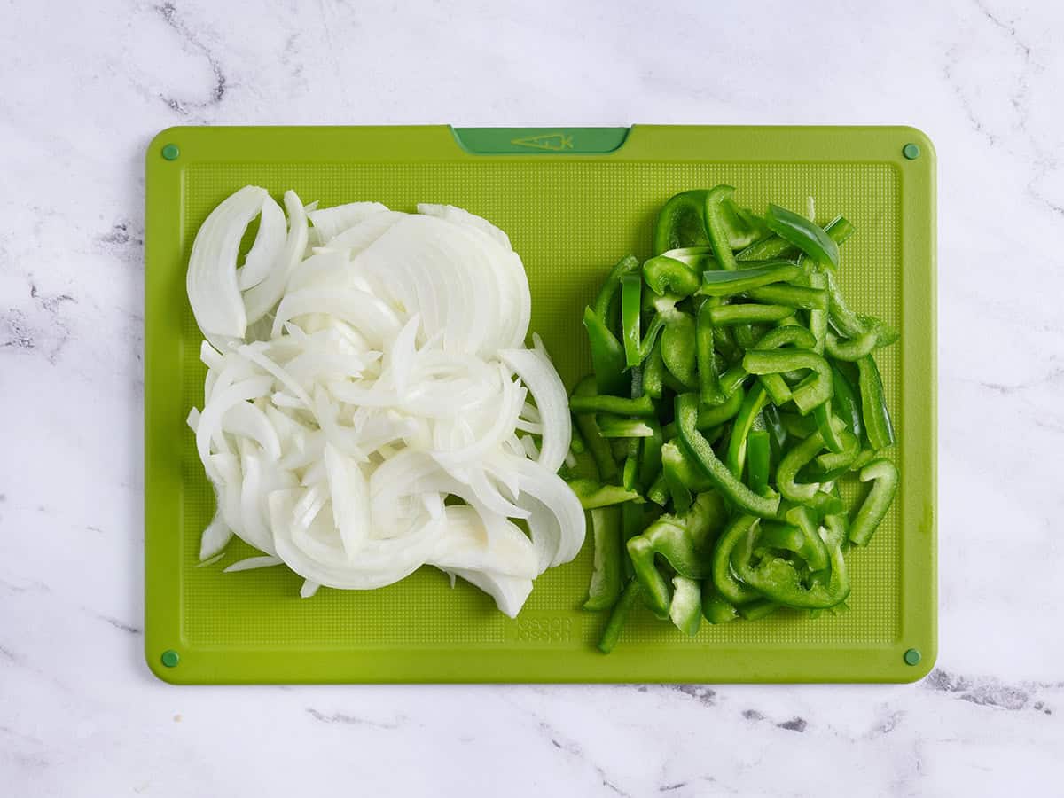Cebollas en rodajas y pimientos verdes sobre una tabla para cortar.