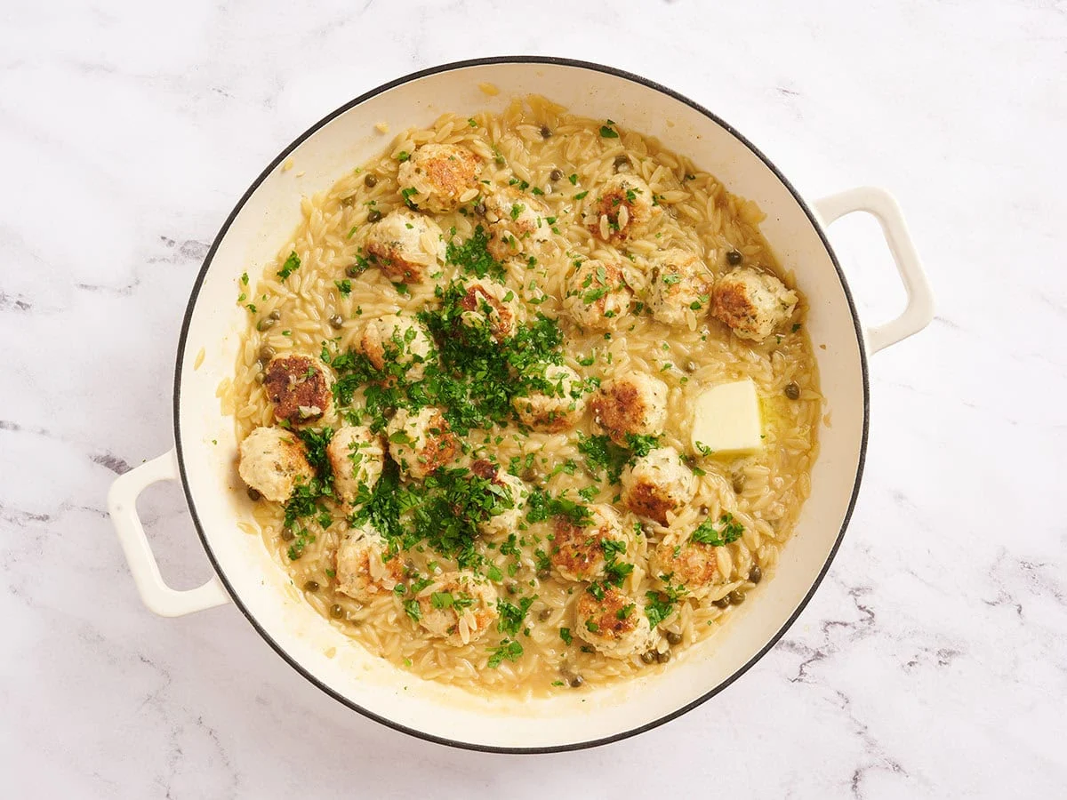 Mantequilla y perejil fresco añadidos a una albóndiga piccata de pollo y una sartén de orzo.