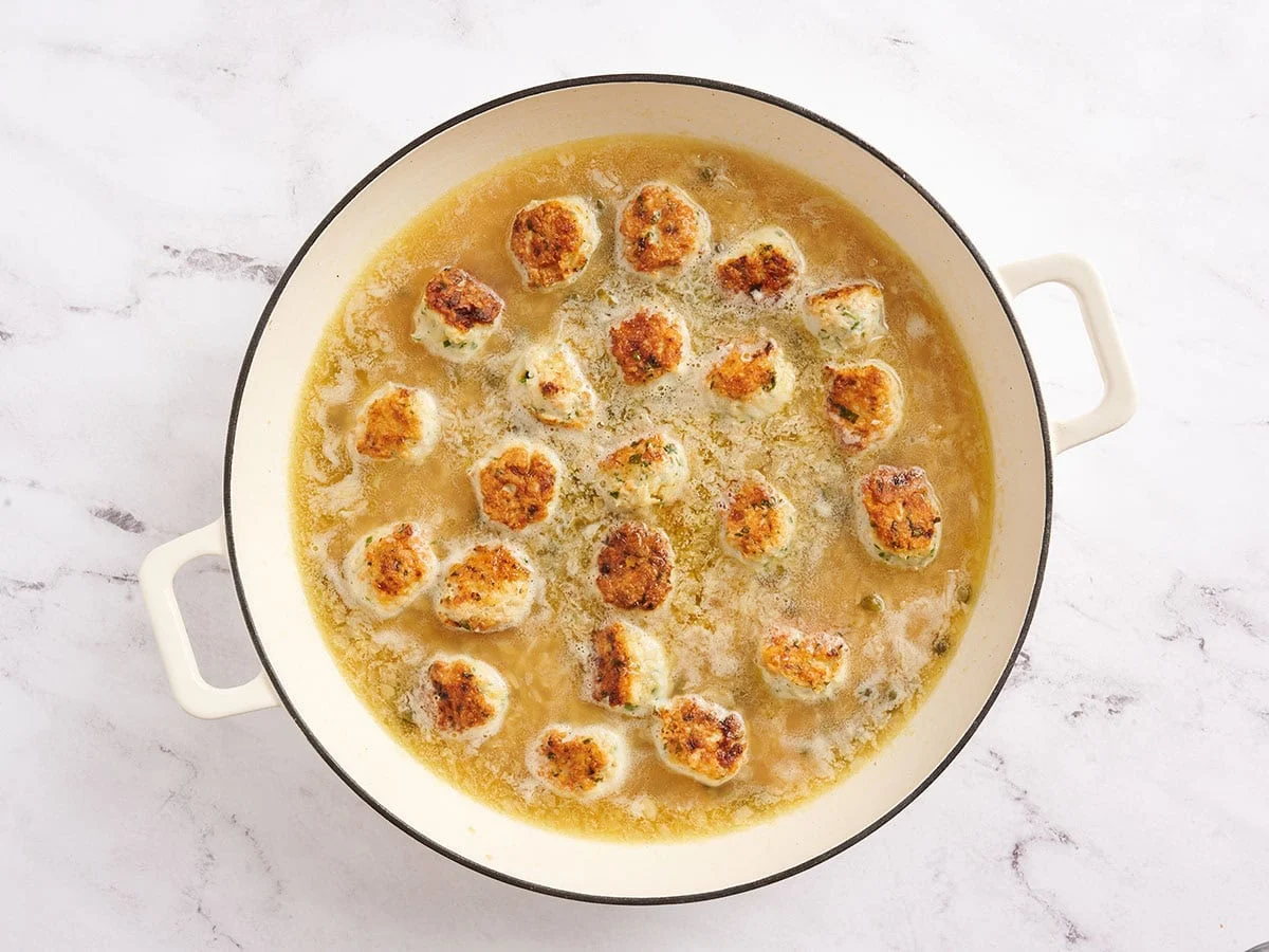 Albóndigas de pollo piccata agregadas a una sartén con orzo y caldo.