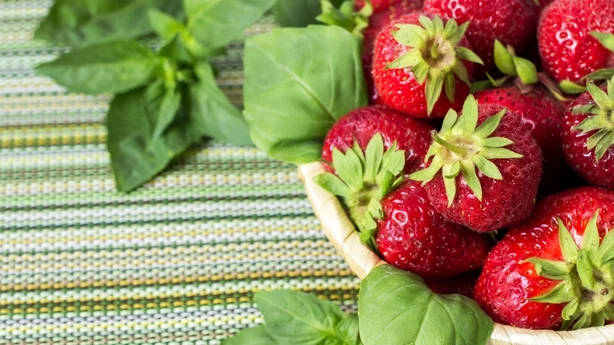 Fresas dulces maduras en cesta de mimbre y hojas de menta sobre fondo de madera