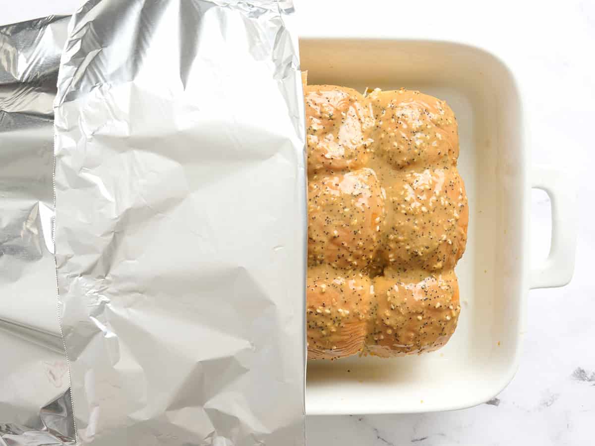 Una fuente para hornear con hamburguesas de pollo cubierta con papel de aluminio.