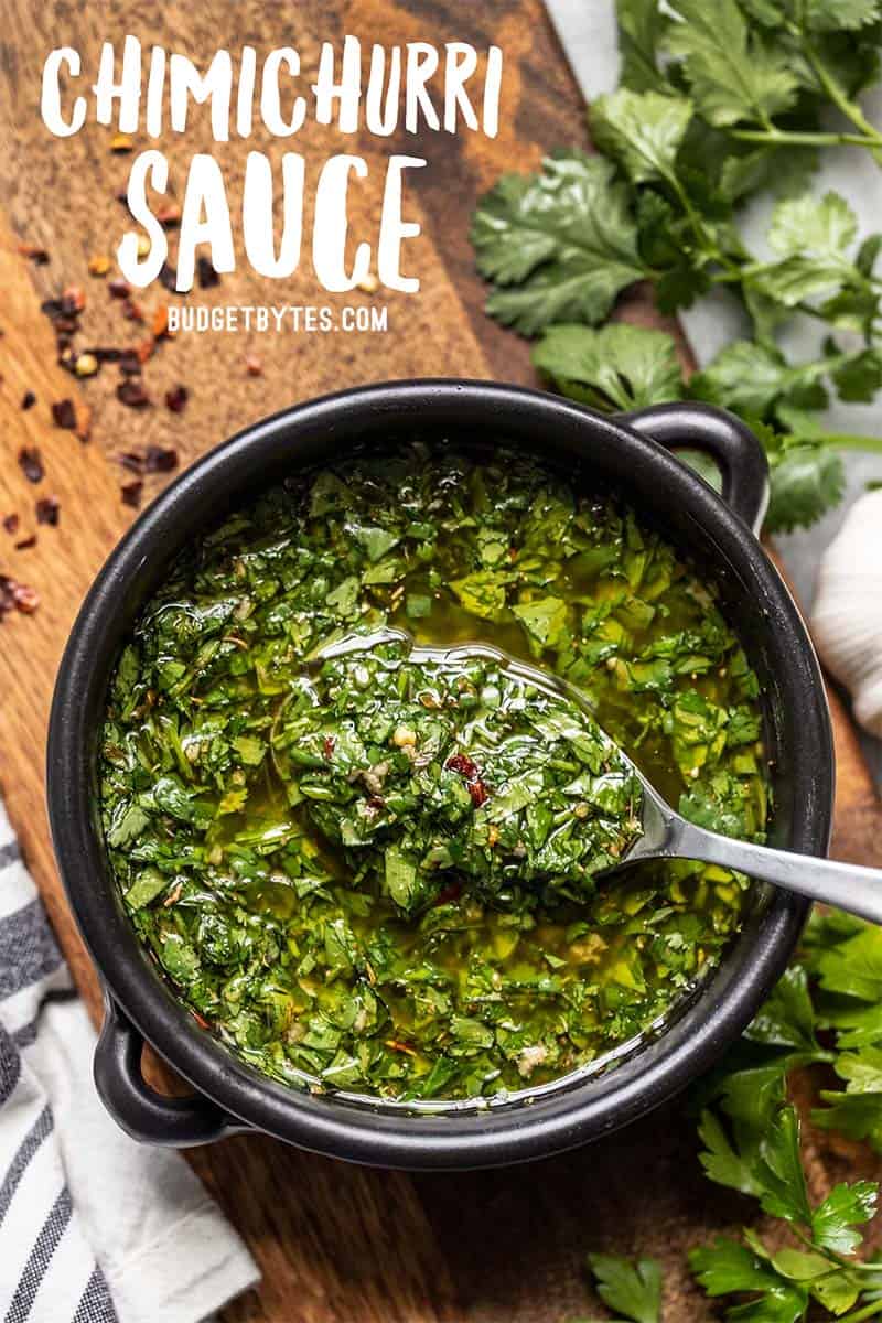 Un tazón negro lleno de salsa chimichurri con una cuchara sacando un poco, de cerca.