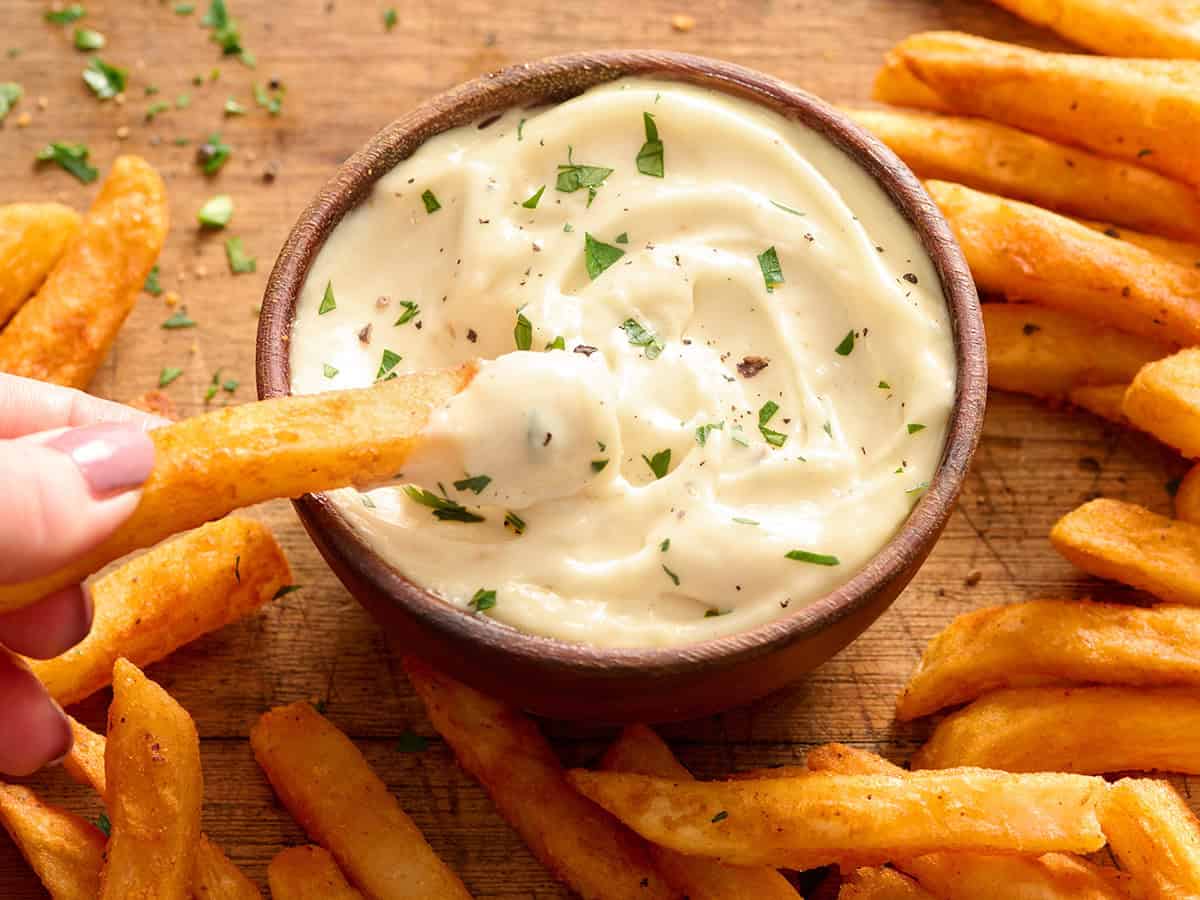 Vista lateral aérea de un plato de alioli de ajo casero con patatas fritas sumergidas en él.