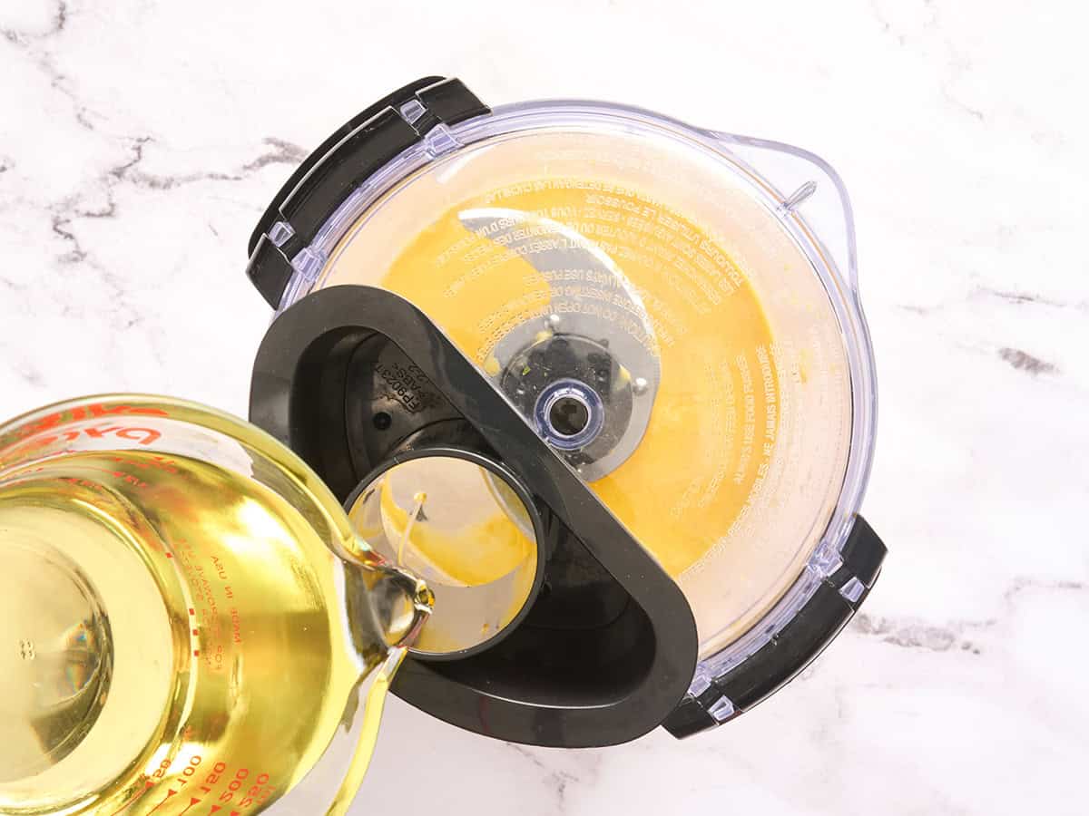 Se vierte aceite en un procesador de alimentos para hacer una emulsión para alioli de ajo.