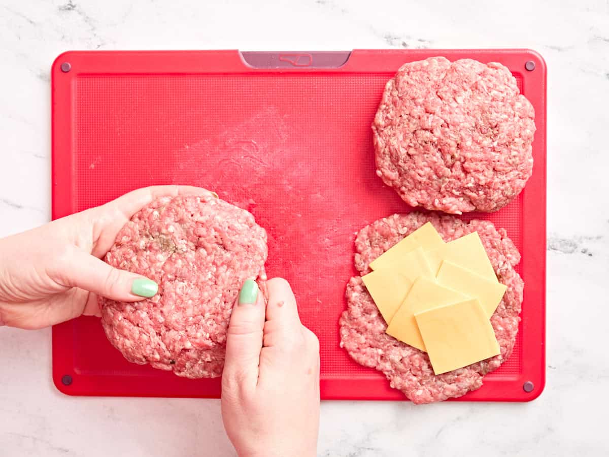 Manos llenando hamburguesas con queso.