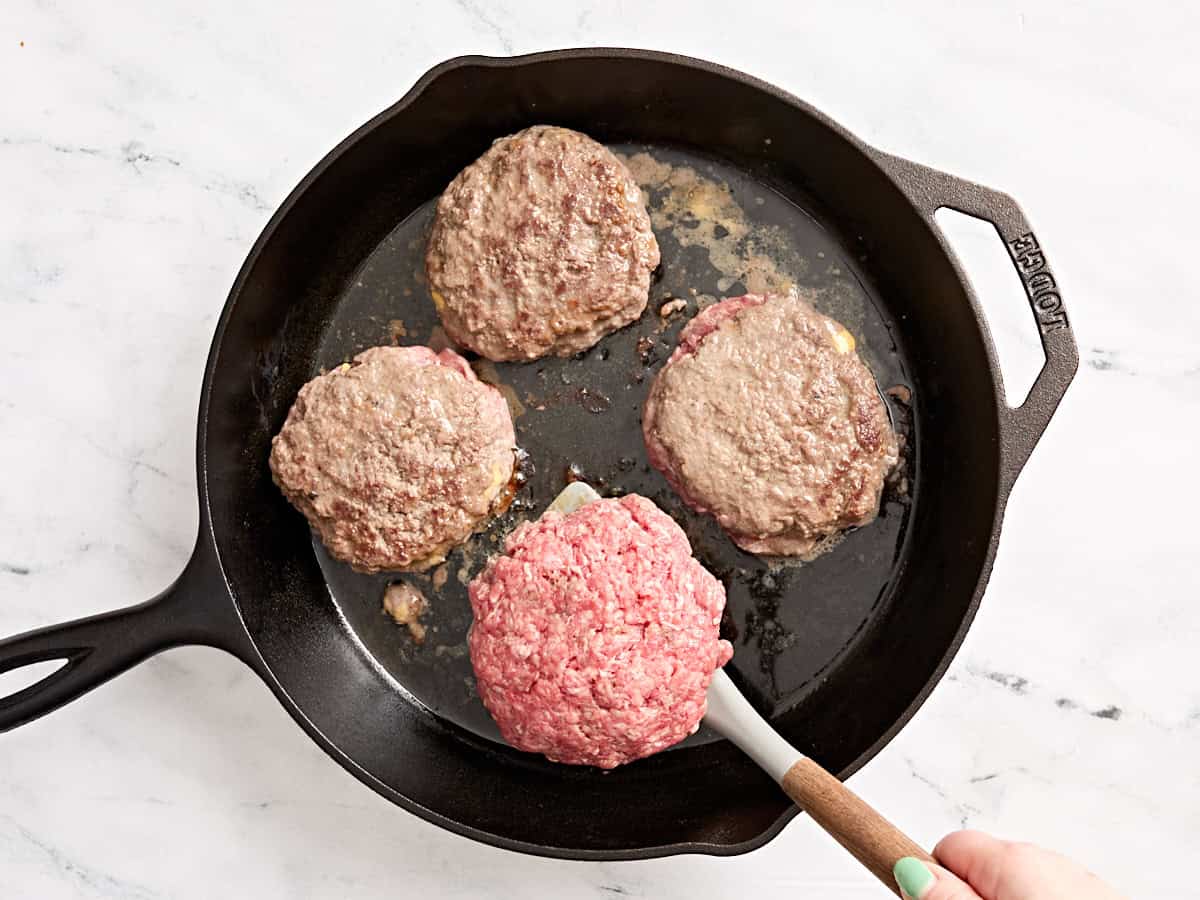 Jugosas hamburguesas Lucy volteadas con una espátula en una sartén.