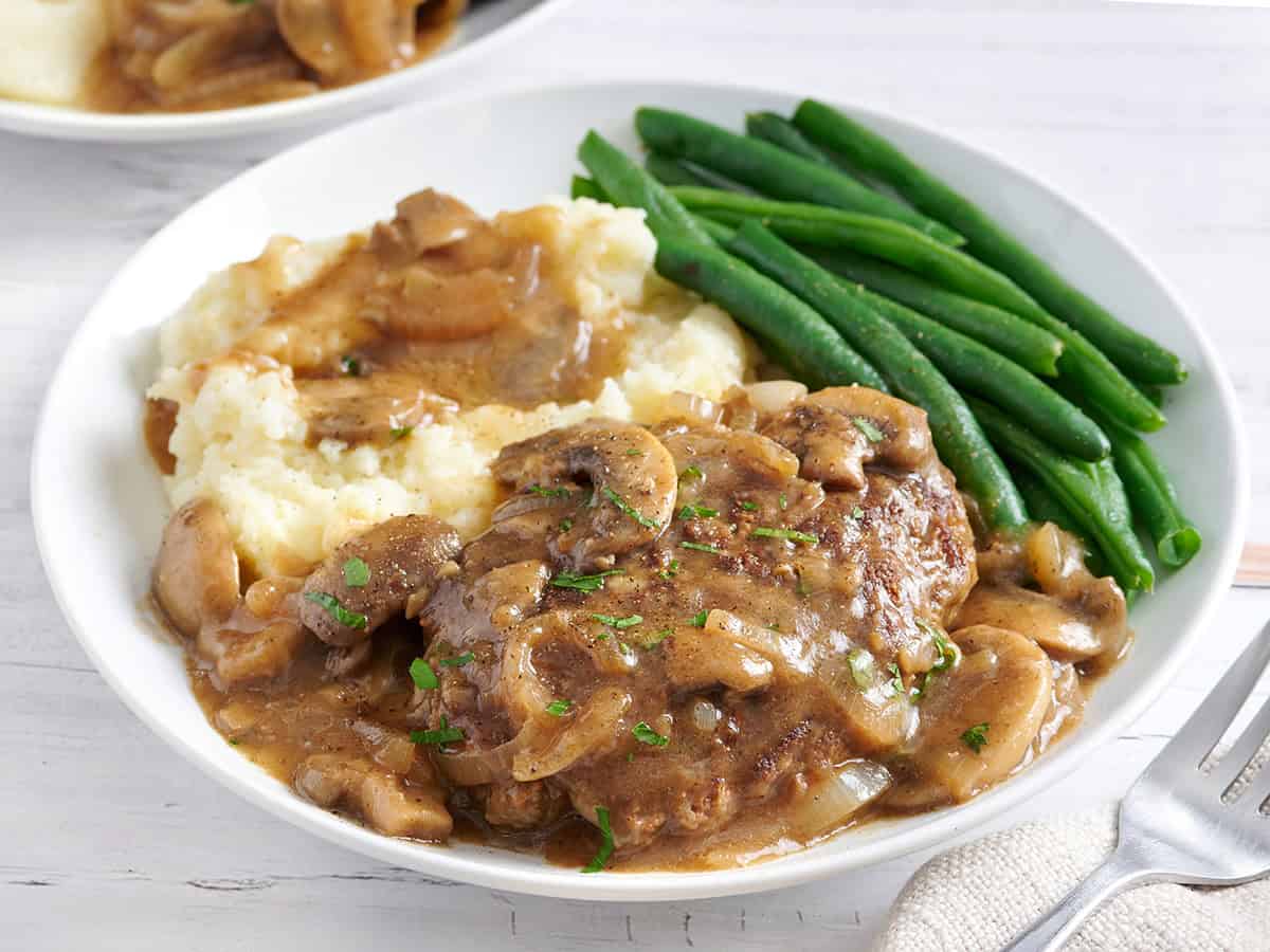 Side view of salisbury steak on a plate with mashed potatoes and green beans.