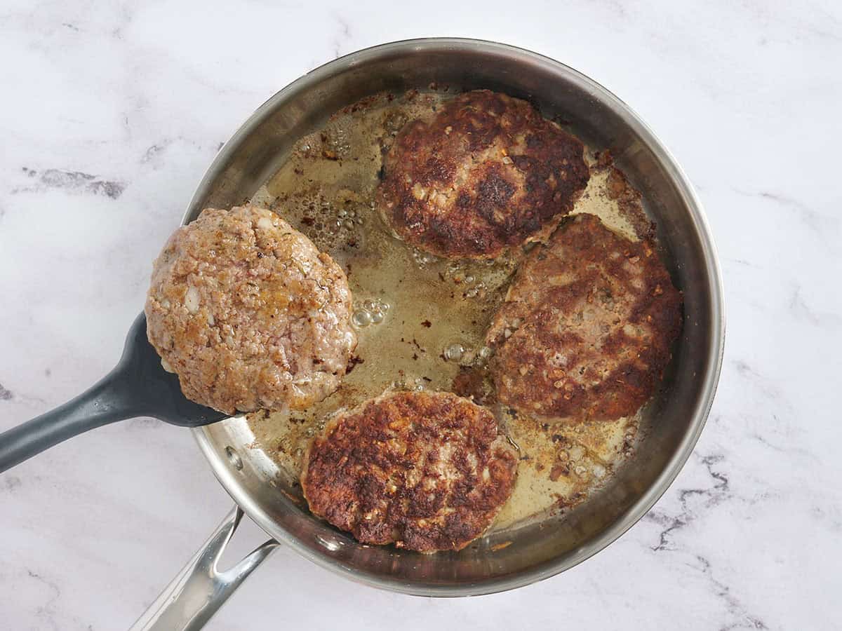 Una espátula para dar vuelta las hamburguesas de filete Salisbury en una sartén.