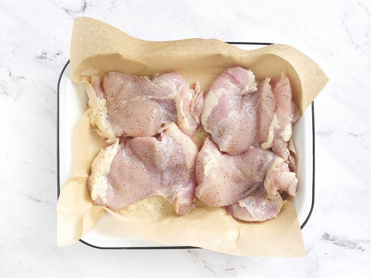 Pollo en una fuente para horno forrada con papel pergamino y cubierto con sal y pimienta.