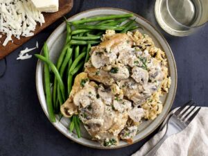 Overhead view of creamy mushroom chicken thighs on a plate with green beans.