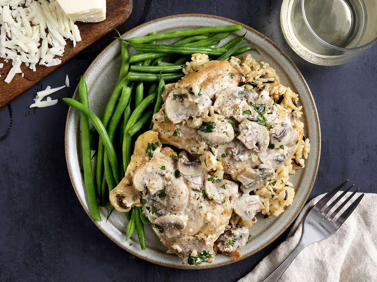 Vista aérea de muslos de pollo cremosos con champiñones en un plato con judías verdes.