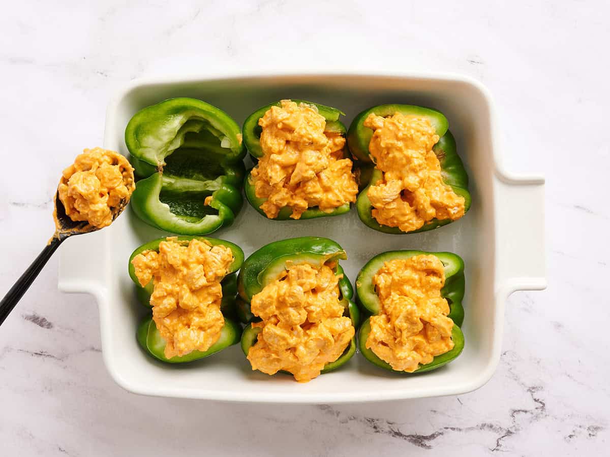 Mitades de pimiento verde en una fuente para horno con relleno de pollo búfalo.