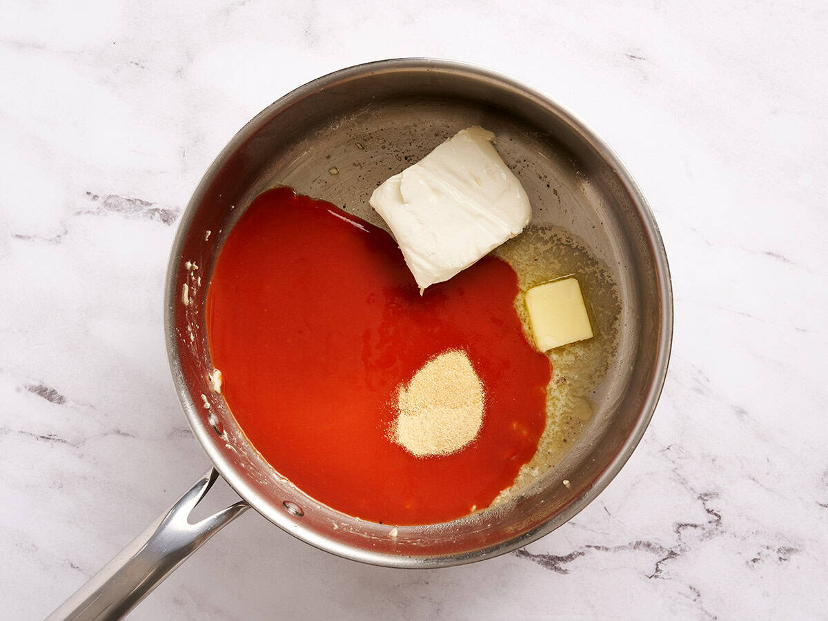 Salsa picante, queso crema, mantequilla y condimentos en una sartén.