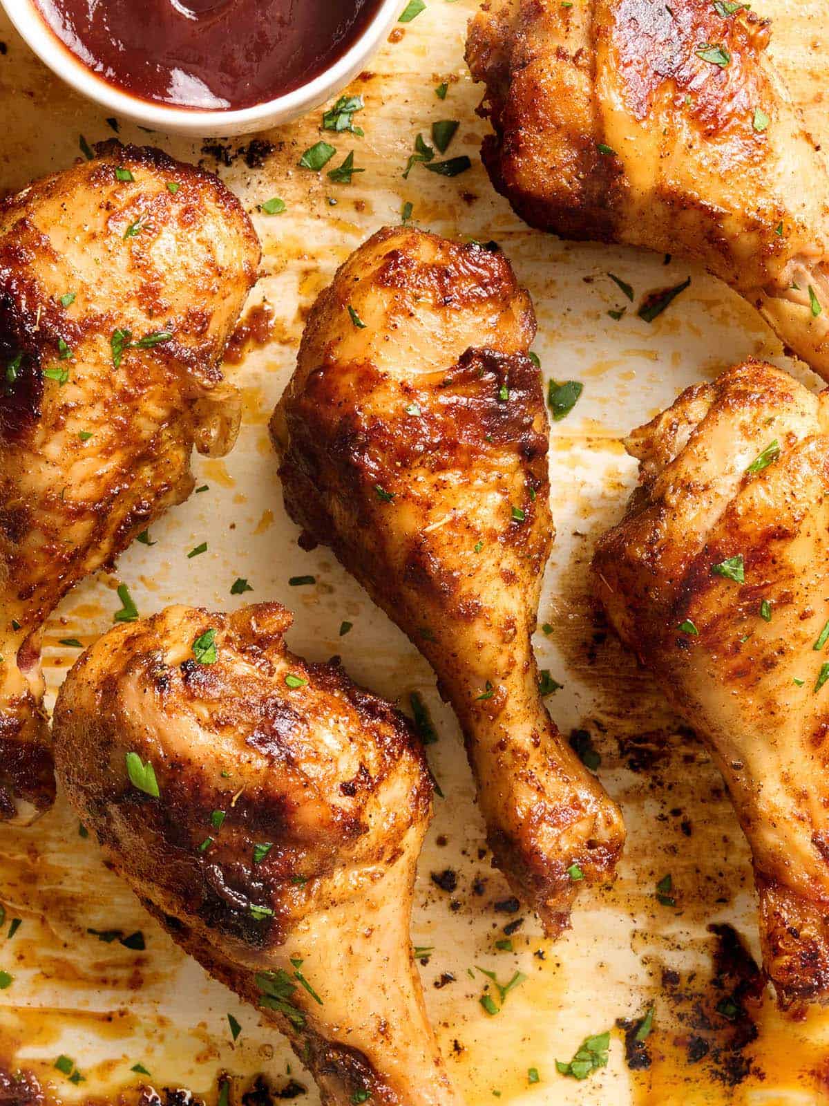 Vista aérea de muslos de pollo al horno en una bandeja para hornear con una olla de salsa BBQ.
