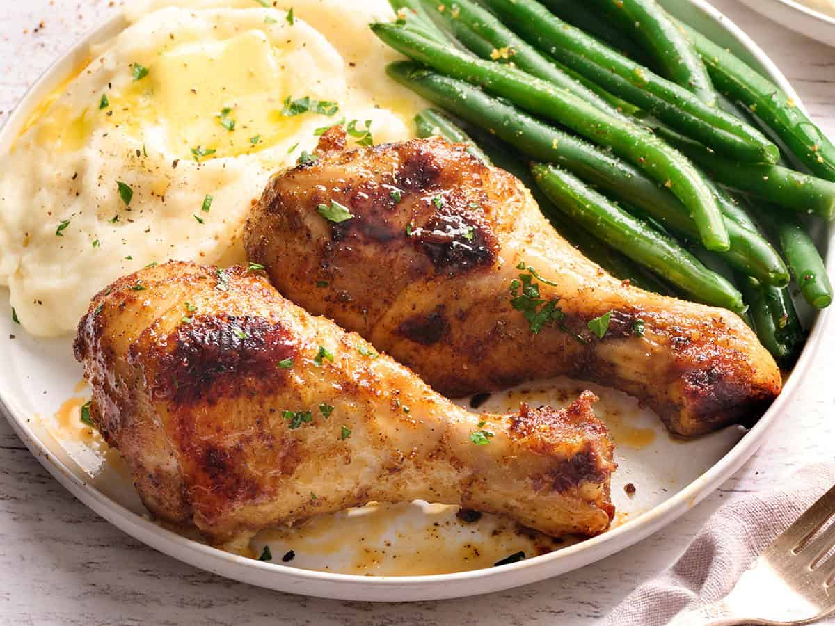 Muslos de pollo al horno en un plato con judías verdes y puré de patatas.