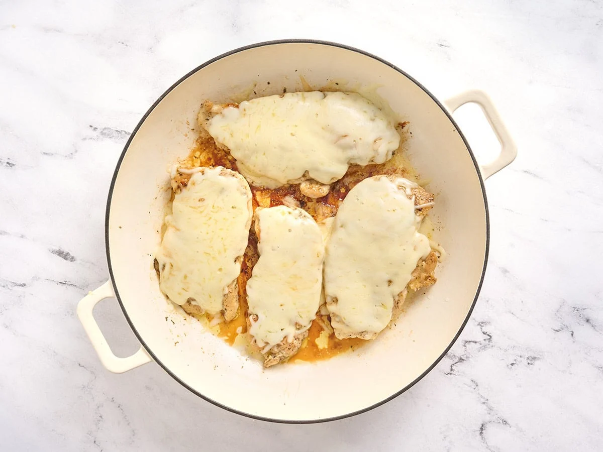 Chuletas de pollo cubiertas con mozzarella derretida en una sartén.