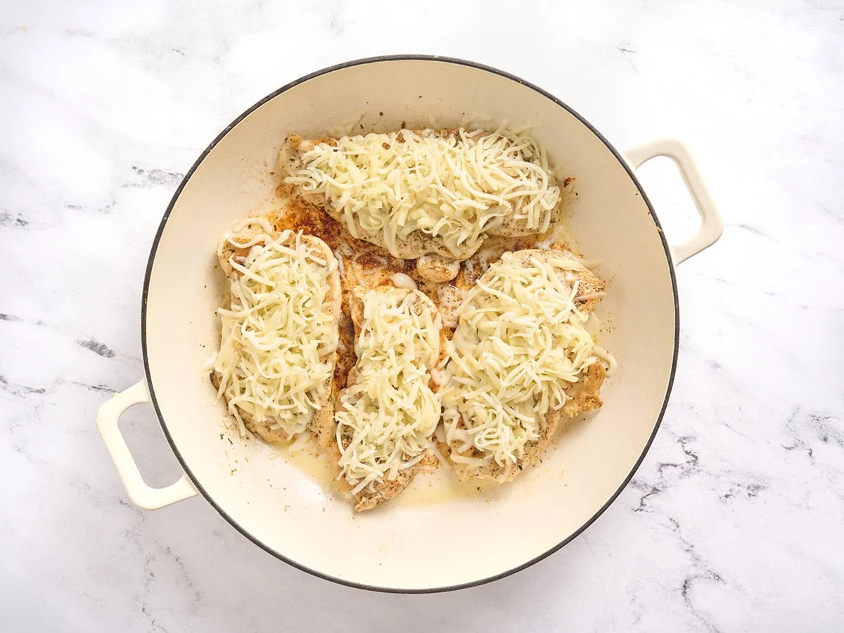 Chuletas de pollo cubiertas con mozzarella en una sartén.