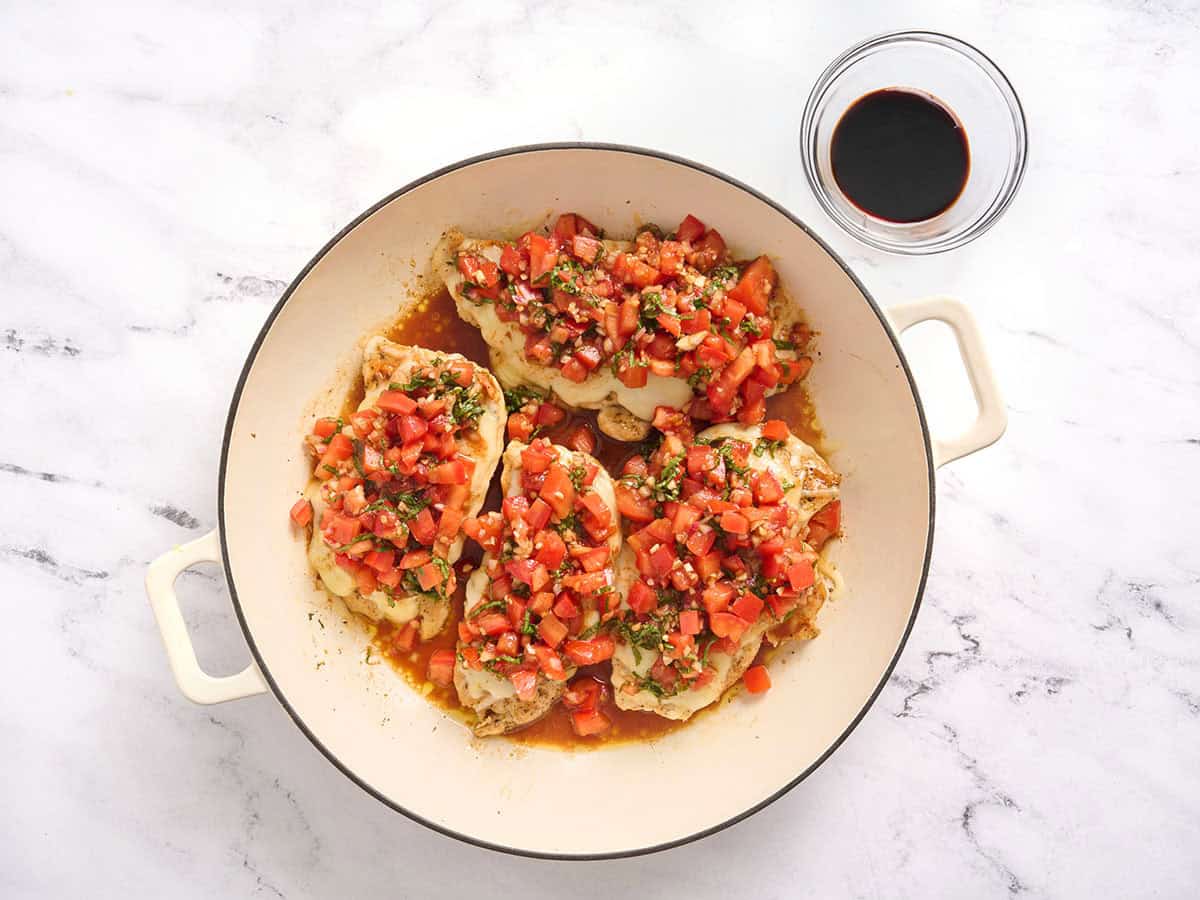 Chuletas de pollo en una sartén cubiertas con bruschetta.