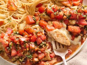 Close up of bruschetta chicken on a plate with a fork and spaghetti.