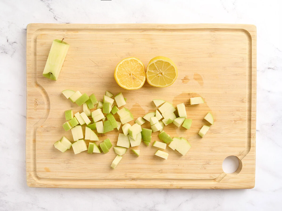 Manzana cortada en cubitos sobre una tabla de cortar con medio limón.