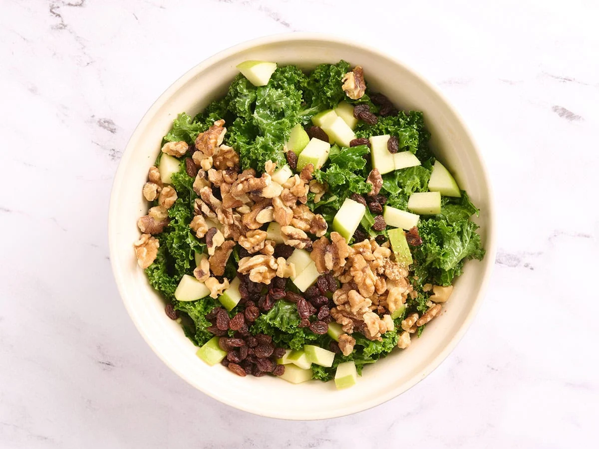 Nueces agregadas a un tazón con ingredientes para ensalada de col rizada.