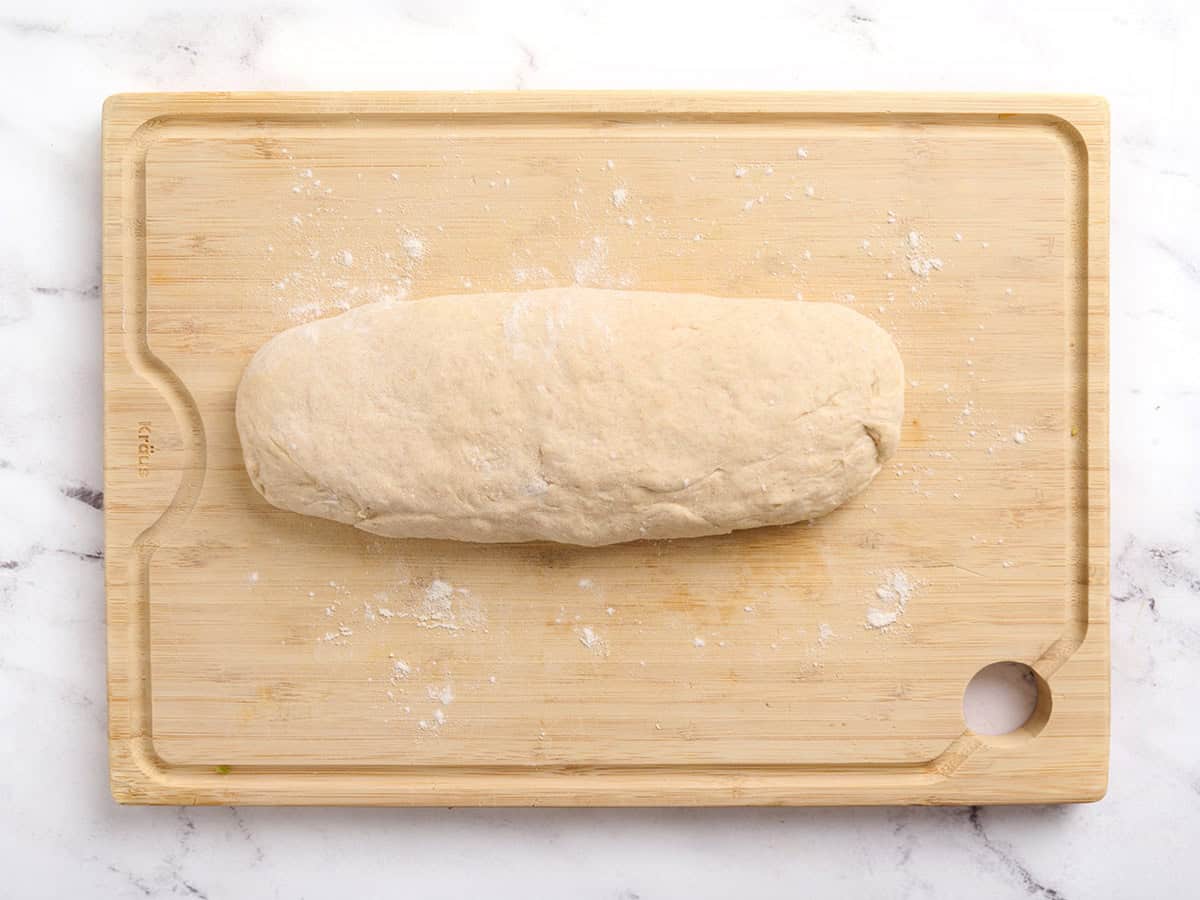 Masa de pan de pita formada en un tronco sobre una tabla de cortar de madera.