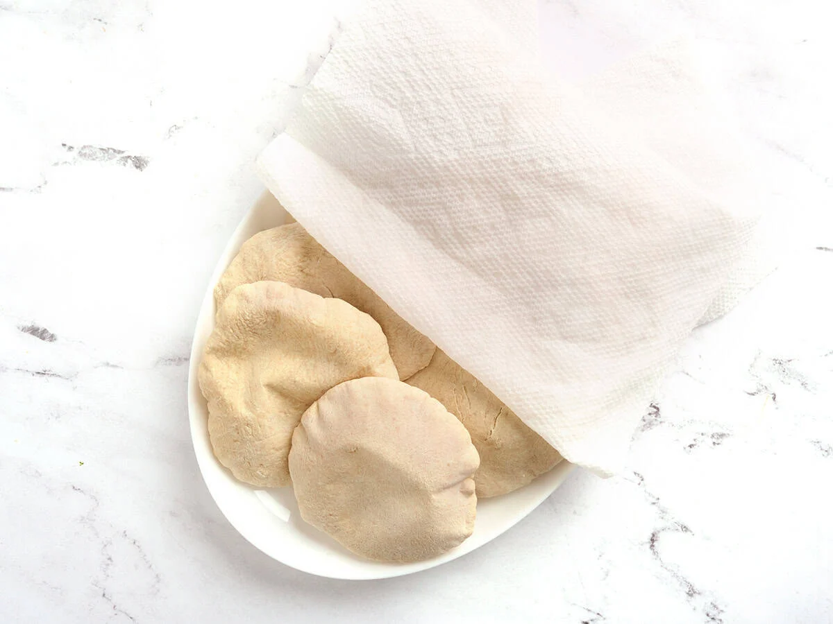 Pan de pita casero en un plato cubierto con un paño húmedo.